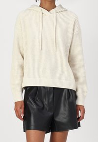 Felpa con cappuccio in maglia color crema con motivo testurizzato, coulisse sul cappuccio e orlo a coste. Abbinata a pantaloncini larghi in pelle nera.