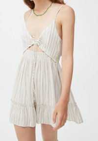 Vestido de lino blanco con tirantes finos, que presenta un corte en la cintura, un lazo en la parte delantera y un sutil patrón a rayas. Dobladillo con volantes y cintura elástica.