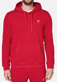 Czerwona bluza z kapturem wykonana z bawełny, z kieszenią kangurką, ściągaczami przy rękawach i u dołu. Mały żółty logotyp na klatce piersiowej dodaje szczegółu.