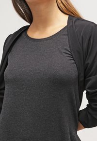 Cardigan nero a maniche lunghe sopra una t-shirt fitted grigia scura. Il tessuto appare morbido con una consistenza liscia; il design è semplice e contemporaneo.