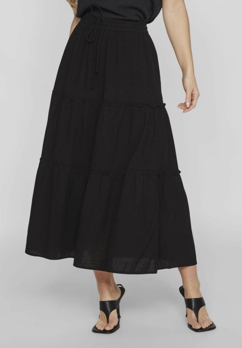 Falda larga negra en capas, hecha de una tela ligera. Presenta una cintura con cordón y un diseño fluido con bordes en forma de ondas.