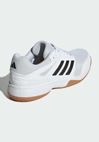 Zapatilla deportiva blanca con parte superior de malla y sintético, que presenta tres franjas negras, una suela de goma y acentos texturizados.