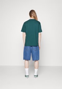Grøn kortærmet t-shirt parret med blå denimshorts, hvide sokker og grønternede slip-on sko. Simpelt design og afslappet pasform.