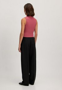 Geknipte, geribbelde tanktop in het roze, gecombineerd met loszittende zwarte broeken. De outfit heeft een elegante, gladde textuur en minimale details.