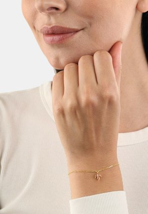 Pulsera de cadena de oro con un pequeño colgante, con una superficie pulida y eslabones delicados, llevada en una mano de piel clara.
