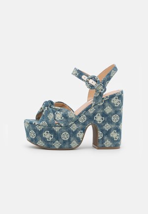 Niebieska sandałka na platformie z kwiatowym i monogramem, pasek wokół kostki z okrągłą klamrą i wysokim, masywnym obcasem.