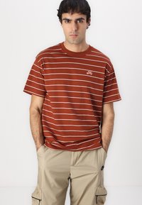 Brun stribet t-shirt med hvide vandrette striber, rund hals og lille Nike-logo, parret med beige cargo bukser.