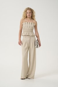 Top beige sans manches avec texture plissée et ourlet volanté, associé à un pantalon taille haute à jambes larges en tissu assorti.