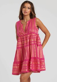 Rosa ärmlös klänning med en djup V-ringning, har guld geometriska mönster, flytande design och flerdelad nederdel. Lättviktsmaterial med en texturerad yta.