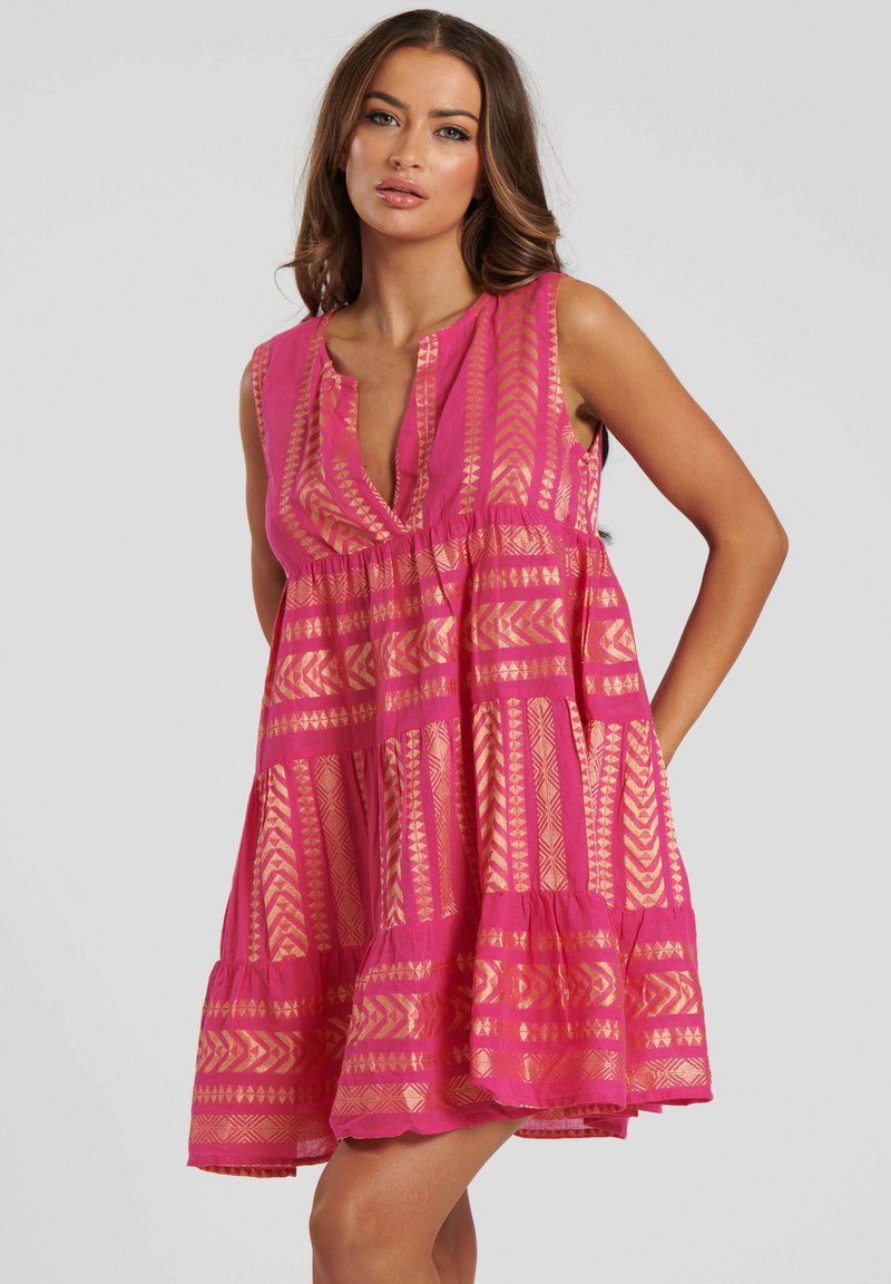 Rosa ärmlös klänning med en djup V-ringning, har guld geometriska mönster, flytande design och flerdelad nederdel. Lättviktsmaterial med en texturerad yta.