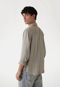 Camisa gris tejida con cuello, mangas enrolladas y un dobladillo ligeramente curvado. Combinada con jeans de mezclilla azul claro.