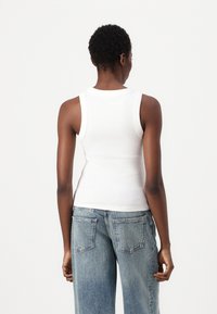 Weißes geripptes Tanktop mit rundem Halsausschnitt und ärmellosem Design, kombiniert mit hellblauen weit geschnittenen Jeans, Ansicht von hinten.