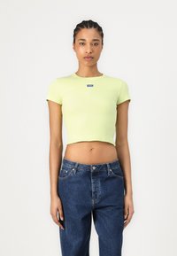 Vaaleanvihreä ribbikuvioinen lyhythihainen crop-top, jossa on pyöreä kaula-aukko ja jonka etuosassa on sininen logopainatus. Yhdistetty tummansiniset farkut.