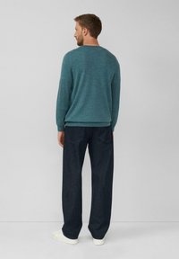 Morska dzianinowa sweter z prążkowanymi mankietami, w połączeniu z ciemnoniebieskimi szerokimi spodniami dżinsowymi i białymi sneakersami. Prosty design, gładka faktura.