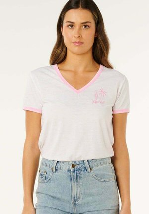 Femme portant un T-shirt blanc à col en V avec un liseré rose et un petit motif de planche de surf rose et de palmier, associée à un jean taille haute bleu clair.