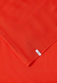 Tissu orange vif avec un coin plié montrant une petite étiquette blanche "CECIL" cousue sur le bord.