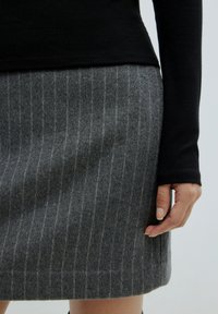 Grauer Wollbleistiftrock mit vertikalen hellgrauen Streifen, kombiniert mit einem eng anliegenden schwarzen Langarmoberteil. Nahaufnahme zeigt Textur und Passform.