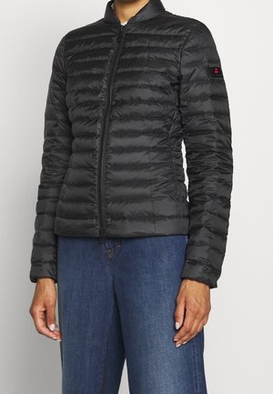 Veste matelassée noire à fermeture éclair portée avec un jean bleu, avec un patch logo visible sur la manche supérieure gauche.