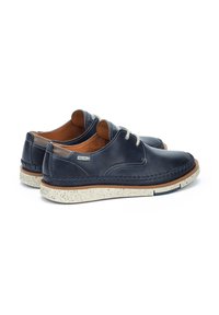 Chaussures en cuir bleu marine avec un design cousu, intérieur beige clair et semelle en caoutchouc blanche et beige tachetée. Présentent des lacets gris.