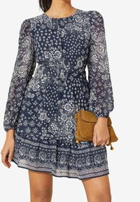 Navy blue floral print dress with long sheer sleeves and belted waist, paired with a small brown suede clutch bag.