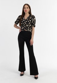 Sort og creme mønstret bluse med puffærmer, parret med højtaljede sorte flared bukser og sorte høje hæle.