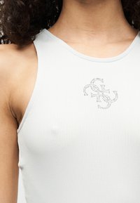 Ανοιχτό γκρι ριμπαρισμένο αμάνικο μπλουζάκι με στρογγυλή λαιμόκοψη, με λαμπερό ασημένιο σχέδιο στο κέντρο. Μαλακή υφή, εφαρμοστή γραμμή.