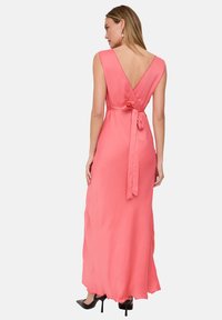 Korallenrotes ärmelloses Maxikleid mit V-förmigem Rücken, Taillenbändern und gewelltem Saum. Hergestellt aus leichtem Stoff mit glatter Textur.