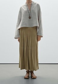 Un haut court rayé gris clair avec un col en V, associé à une jupe maxi plissée beige. Des sandales brunes à lanières complètent la tenue.