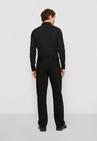 Camisa negra de manga larga y jeans negros. La camisa presenta un cuello y puños abotonados; los jeans tienen un corte clásico y un diseño de cinco bolsillos.