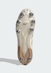 Fotbollsskon sula, genomskinligt vitt material, sex metallspikar, strukturerat greppmönster och en ljusbrun detalj nära hälen.