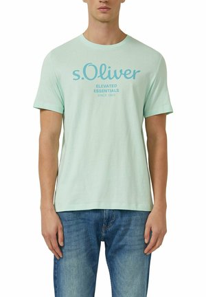 Homme portant un t-shirt vert clair de la marque s.Oliver avec l'inscription « ELEVATED ESSENTIALS SINCE 1969 », associé à un jean bleu.