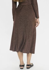 Frau von hinten betrachtet, die ein glitzerndes braunes Midikleid mit langen Ärmeln und schwarze flache Sandalen mit Riemen trägt.