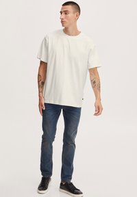 Hvid t-shirt i bomuld med rund hals og korte ærmer, kombineret med blå denimjeans og sorte sneakers. Enkel, afslappet pasform.