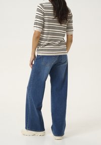 T-shirt en tricot rayé beige avec des rayures noires, associé à un jean en denim bleu à jambes larges. Des sneakers à semelle blanche texturée complètent le look.