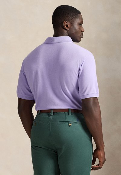 Μωβ πόλο μπλούζα κοντού μανικιού με υφή, συνδυασμένη με πράσινο παντελόνι. Διαθέτει γιακά και καφέ ζώνη με χρυσή λεπτομέρεια.