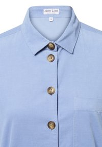 Light blue corduroy shirt with a pointed collar, featuring a pocket and brown buttons down the front. Label reads "Marie Lund, Copenhagen."
