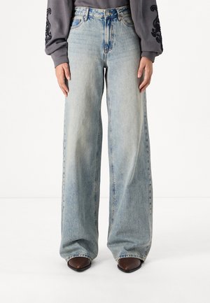 Lichtblauwe wijdvallende jeans met een vervaagde afwerking, hoge taille en een vijf-pocket ontwerp, gecombineerd met donkerbruine schoenen met een puntige neuzen.