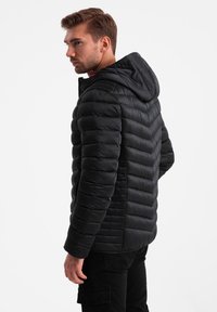 Schwarze Jacke im Puffer-Stil mit horizontalem Steppmuster, Kapuze und roten Kordelzügen, gefertigt aus glänzendem, isoliertem Material.