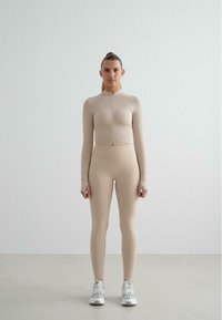 Beige athletic set featuring a fitted long-sleeve top with a front zipper and high-waisted leggings, paired with gray and white sneakers.