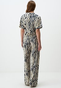 Zebra print jumpsuit in ivoor en marineblauw; lichtgewicht stof, korte mouwen, elastische tailleband, wijde pijpen, zichtbare naden.