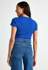 Blå, ribbet kortærmet top kombineret med højttaljede blå denimjeans med to baglommer og løs pasform.