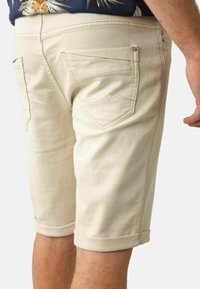 Beige denim shorts met een opgerolde zoom, voorzien van achterzakken met gestikte accenten en een gladde textuur. Geen zichtbare hardware aan de voorkant.