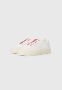 Hvite kanvas sneakers med rosa snørebånd, rund tå og tykk kremfarget såle. Har enkle sømdetaljer på sidene.