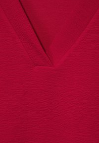 Gros plan d'un tissu rouge texturé avec un détail d'encolure en V sur un vêtement.