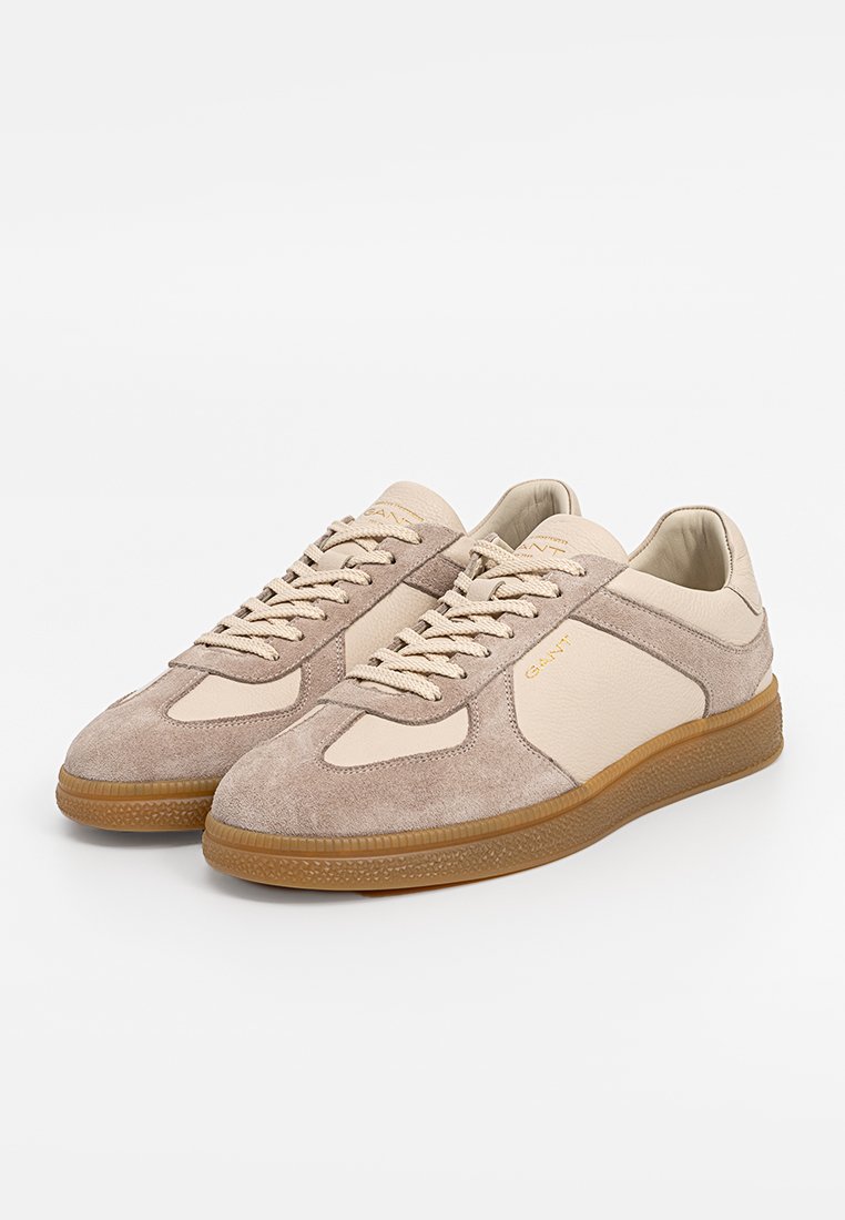 Beige Wildleder- und Leder-Sneaker mit Gummisohle, die ein klassisches Schnürdesign und kontrastierende Texturakzente aufweisen.
