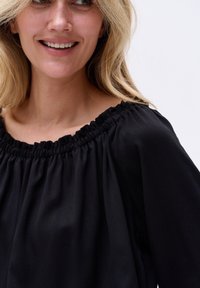 Schwarze Bluse mit lockerer Passform, gerafftem Ausschnitt und glatter Textur. Hat weite Ärmel und dezente Drapierung.