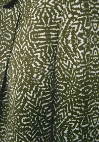 Mönstrad tyg med en texturerad olivgrön bas och vita abstrakta mönster. Intrikata mönster skapar visuell djup och komplexitet.