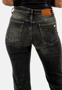 Jeans in denim nero con un design aderente, dotati di una toppa in pelle marrone etichettata "PLEASE" e distinti punti di cucitura sulle tasche posteriori.