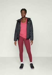 Doudoune noire, débardeur rose, leggings bordeaux. Comprend une capuche, coupe slim et logos sur la doudoune et le débardeur. Baskets noires avec accents blancs.