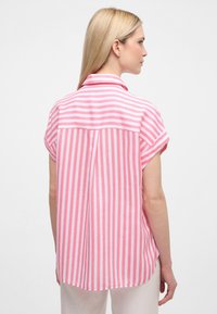 Camicia a maniche corte con colletto, caratterizzata da righe verticali rosa e bianche, con un retro a yoke e una vestibilità rilassata, realizzata in tessuto leggero.